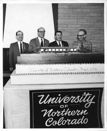 Four men stand behind a cake with a diorama of Michener Library on top, Charter Day, May 1, 1970
